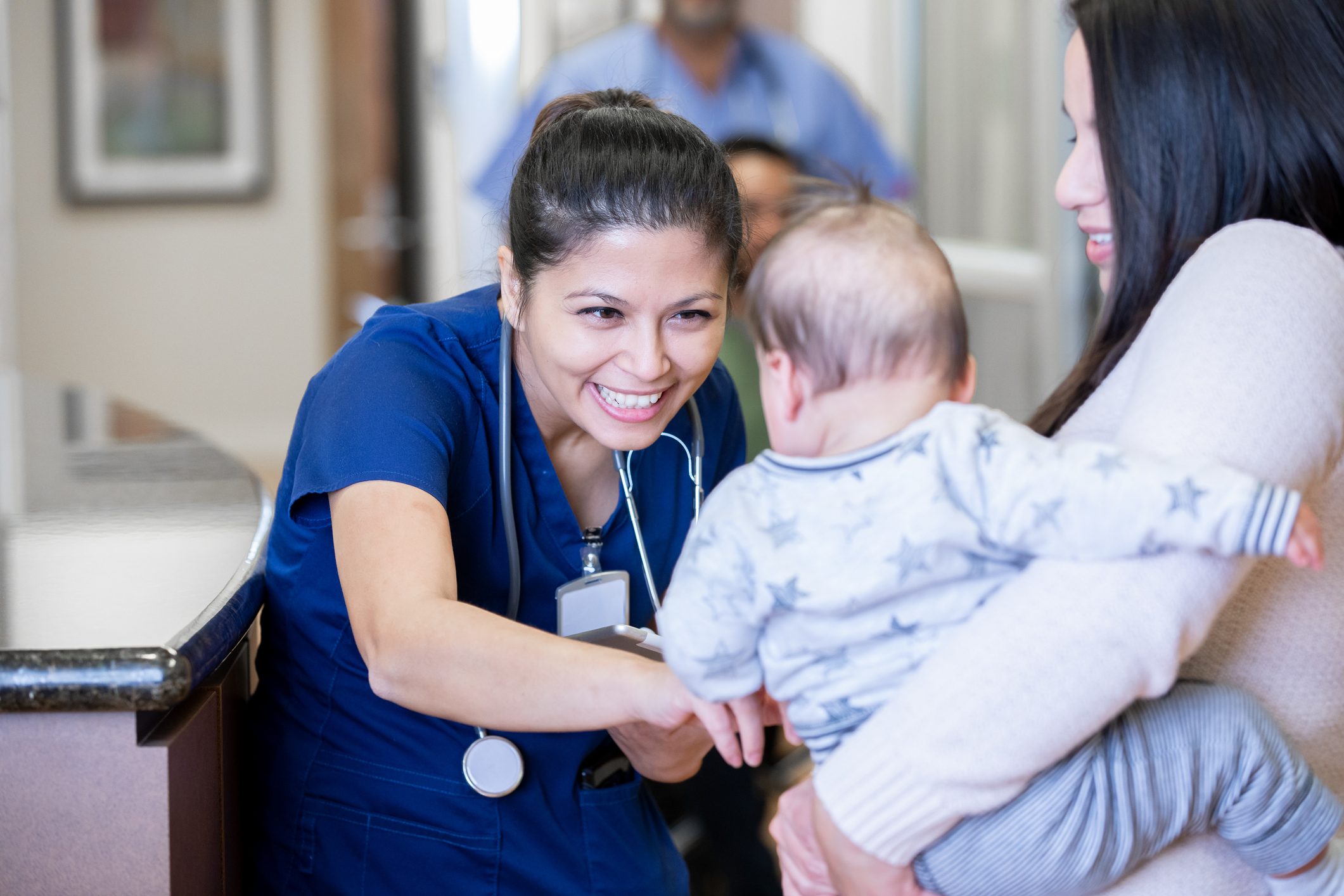 Healthcare professional interacting with a baby held by an adult.