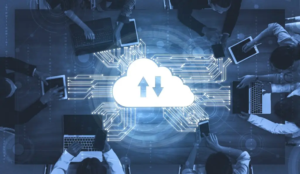 A team collaborating around a table with digital devices, symbolizing cloud computing and data sharing.