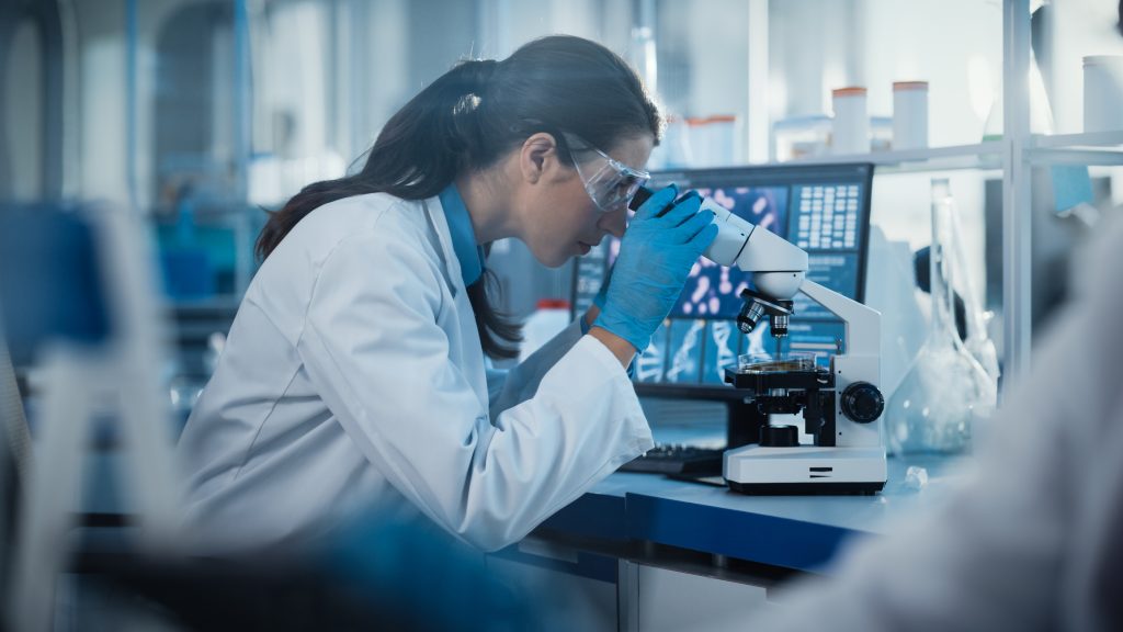 A woman is looking through a microscope in a laboratory.