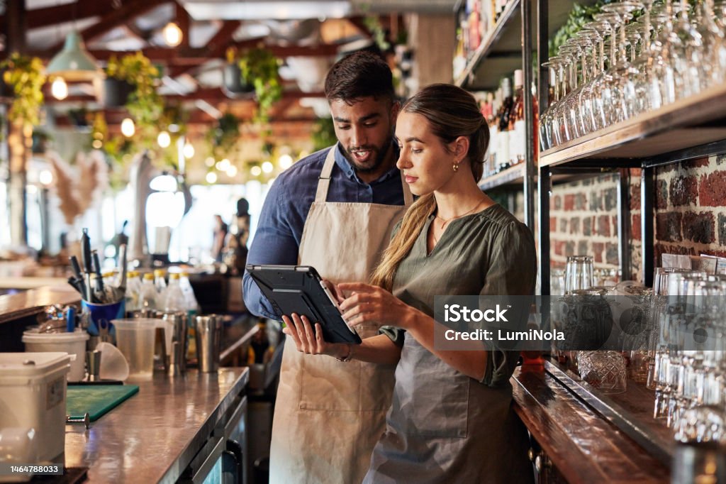 Deux baristas en tablier utilisant une tablette numérique dans un café moderne.
