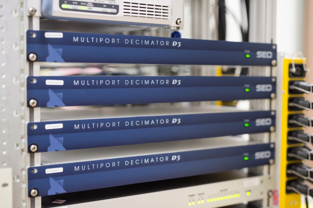 Four blue Multiport Decimator D3 units are installed in a rack, each labeled with the model and manufacturer's logo, and connected to various networking equipment.