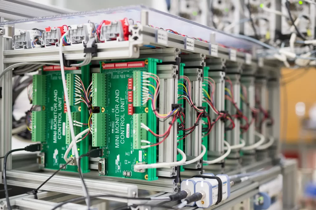 Close-up of a rack with multiple green circuit boards connected by numerous wires in a technological setting.