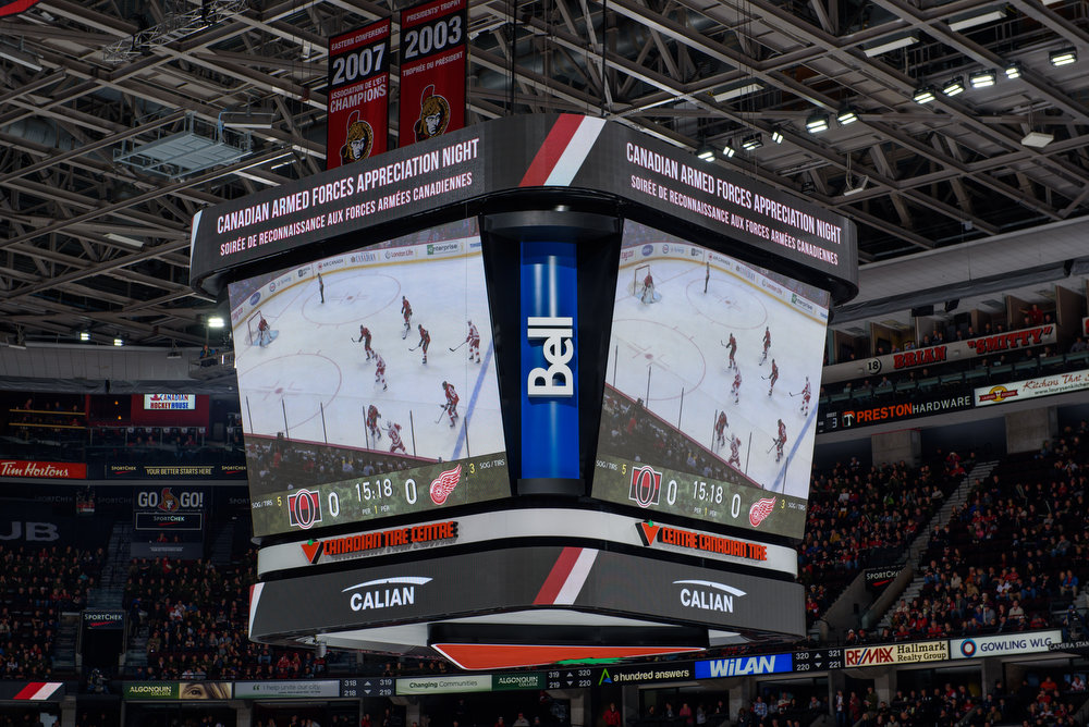 Grand écran Jumbotron dans une arène de hockey affichant un match en cours et un message sur la soirée de reconnaissance des Forces armées canadiennes. L'arène est remplie de spectateurs.