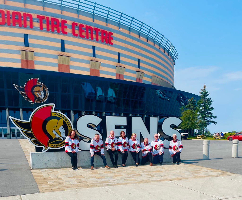 Un groupe de personnes portant des maillots des Sénateurs d'Ottawa pose devant le panneau « Sens » à l'extérieur du Centre Canadian Tire.