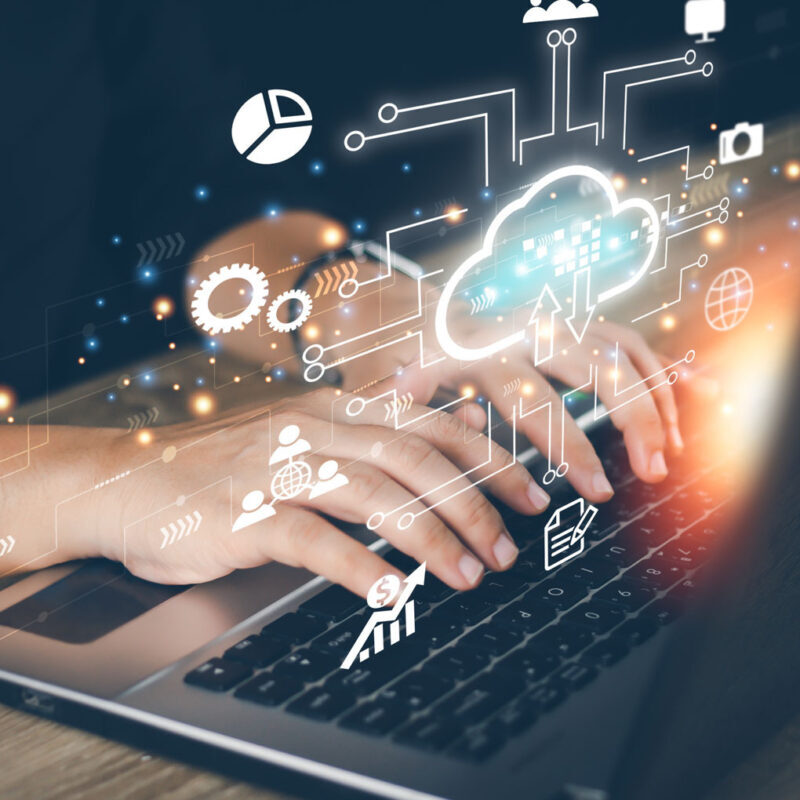 Hands typing on a laptop keyboard, with digital icons representing cloud computing, graphs, and data sharing overlayed above.