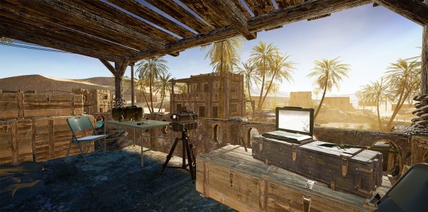 A rustic outdoor workspace with wooden crates, folding chairs, a tripod, a laptop, and tools, set in a desert environment with palm trees and old buildings in the background.